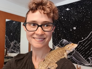 Dawn Beamer smiling. A bearded dragon sits on their shoulder.