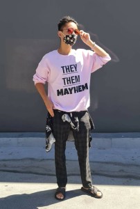 Jordan Phillips wearing a pink sweater that reads "They/Them Mayhem" and looking super cool.